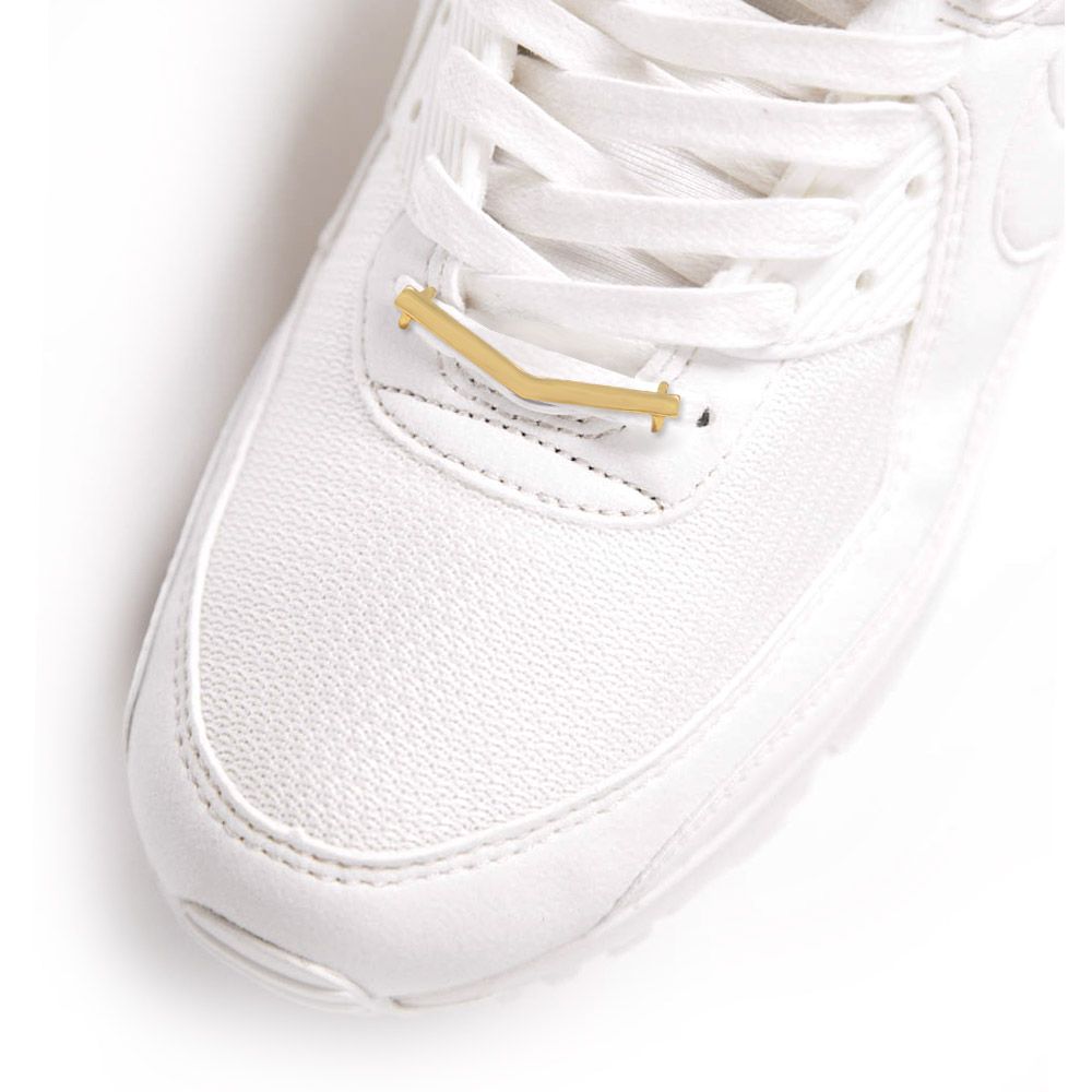 Primo piano di un elegante ciondolo per scarpe placcato oro a forma di V attaccato ai lacci di una sneaker bianca, che mostra un accessorio di moda unico.
