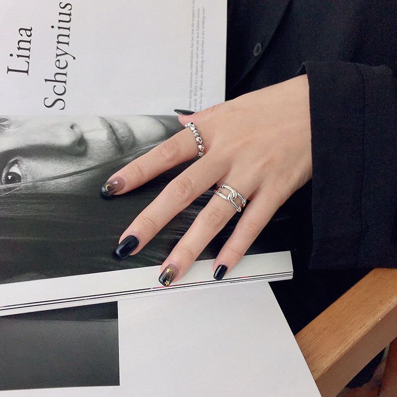A woman's hand with black nail polish wearing a set of five 925 sterling silver minimalist rings, resting elegantly on a magazine.