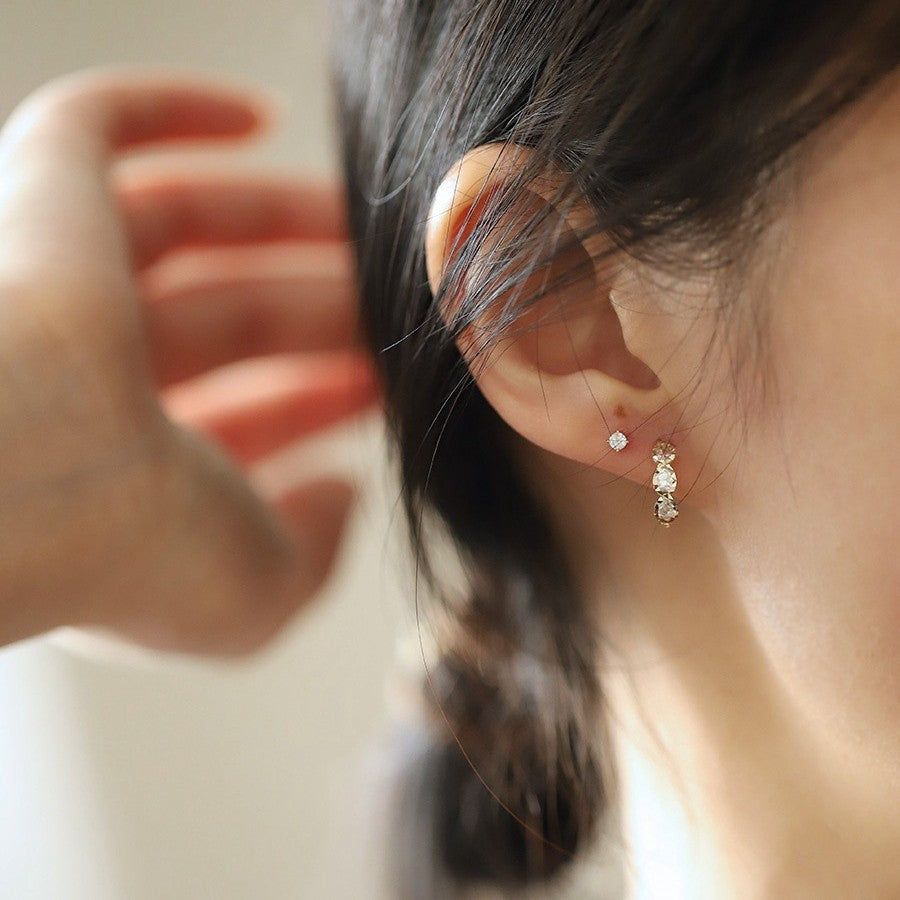 A close-up of a woman wearing the elegant 925 sterling silver 14K gold plated triple teardrop CZ huggie earrings.