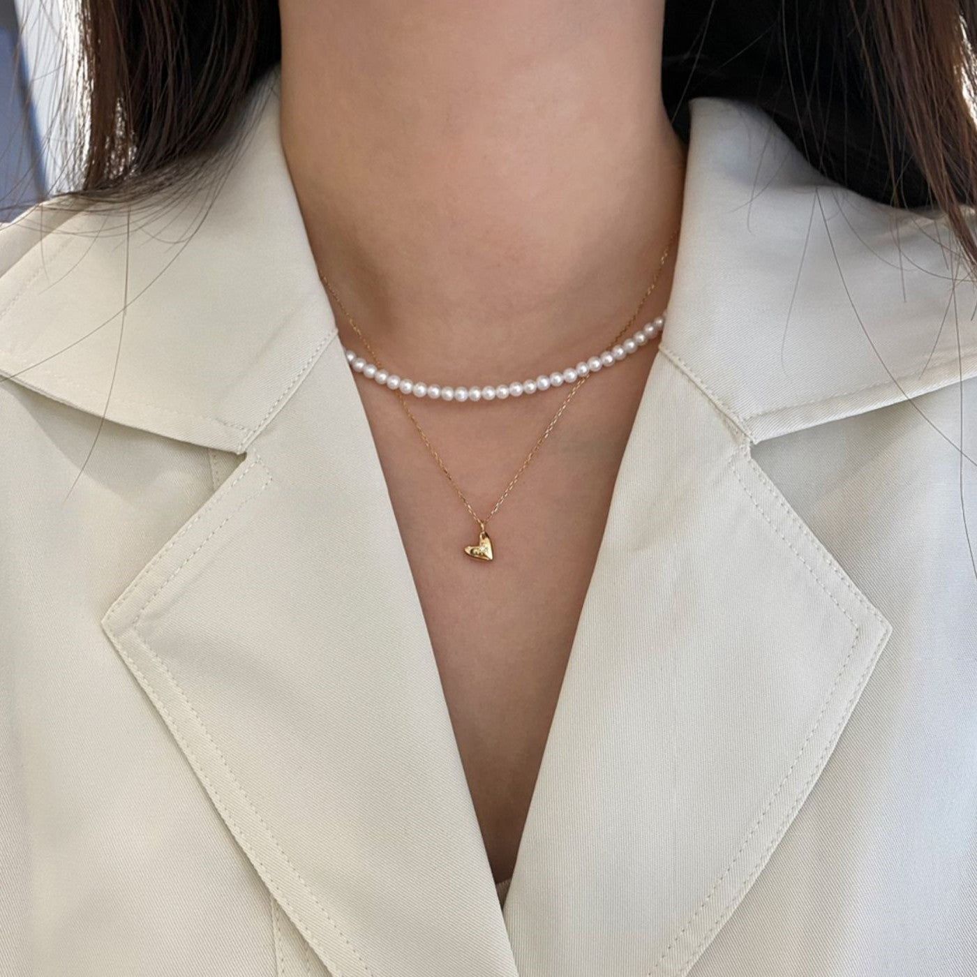 Una mujer que lleva un elegante collar de corazón chapado en oro de 18K y plata esterlina 925 con un diseño de explosión de estrellas, superpuesto con un collar de perlas.