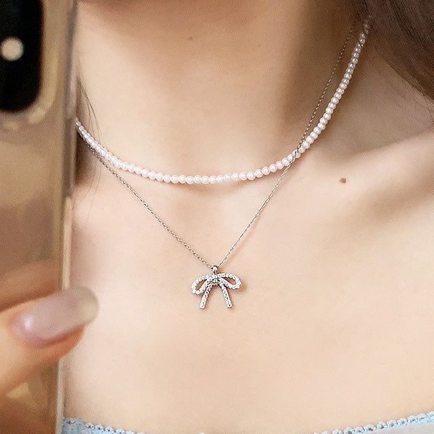 Un modèle portant un élégant collier en argent sterling 925 avec nœud en zircon étincelant, superposé à un choker en perles. Une pièce de bijouterie en gros de JR Fashion Accessories.