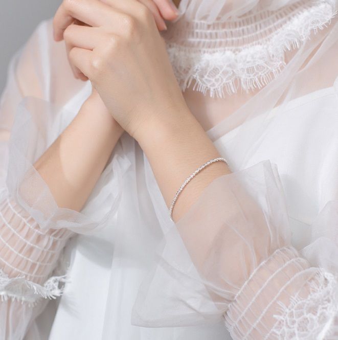 Een close-up van een vrouw die de elegante 925 Sterling Zilveren Glanzende Armband draagt, waarbij het handgemaakte ontwerp tegen een witte jurk wordt getoond.