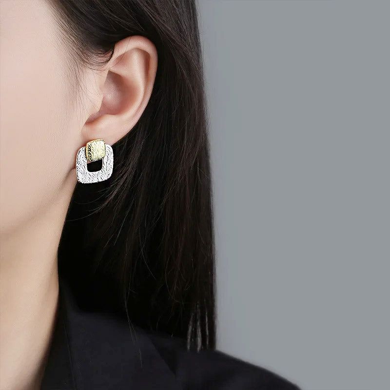 Un primo piano di una donna che indossa l'orecchino a bottone quadrato cavo geometrico bicolore in argento sterling 925, evidenziando il suo design elegante.