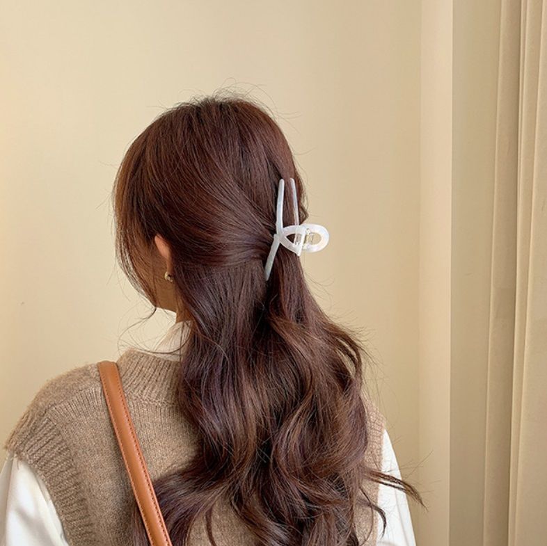 Una donna con capelli biondi che indossa un outfit beige, mostrando un grande fermaglio per capelli in acetato bianco in una elegante coda di cavallo bassa.