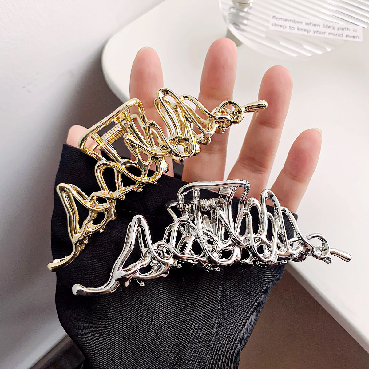 A set of metal alloy hollow geometric hair claw clips, showcasing both the gold and silver finishes held by a gloved hand.