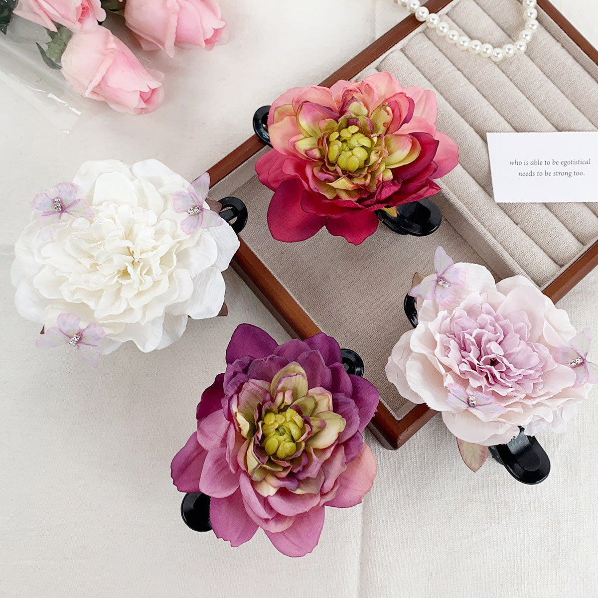 A collection of beach vacation style artificial peony and lotus flower claw hairclips displayed on a decorative board, showcasing various colors.
