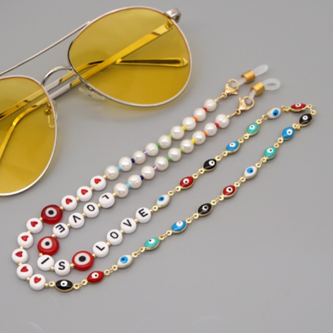 A stylish gold-plated Evil Eye beaded chain shown attached to a pair of sunglasses, serving as a fashionable eyewear strap.