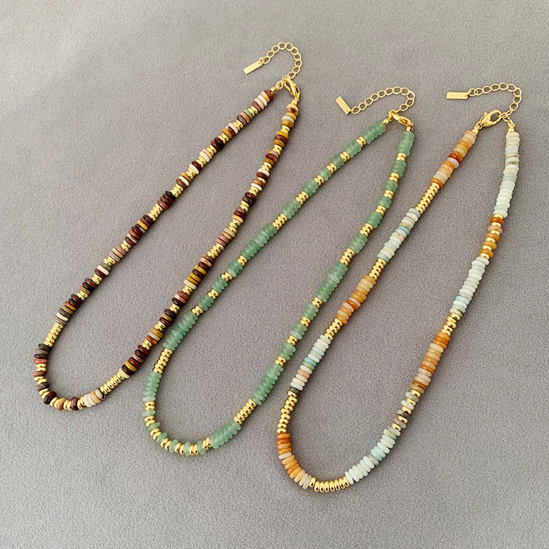 A set of three boho-style brass and natural bead necklaces in vibrant orange, brown, and green color schemes, displayed on a neutral background.