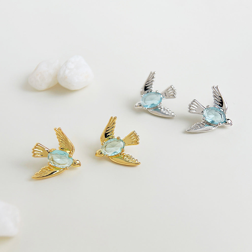 A pair of gold and silver 3D bird stud earrings with delicate light blue crystal stones, offered by JR Fashion Accessories for wholesale.