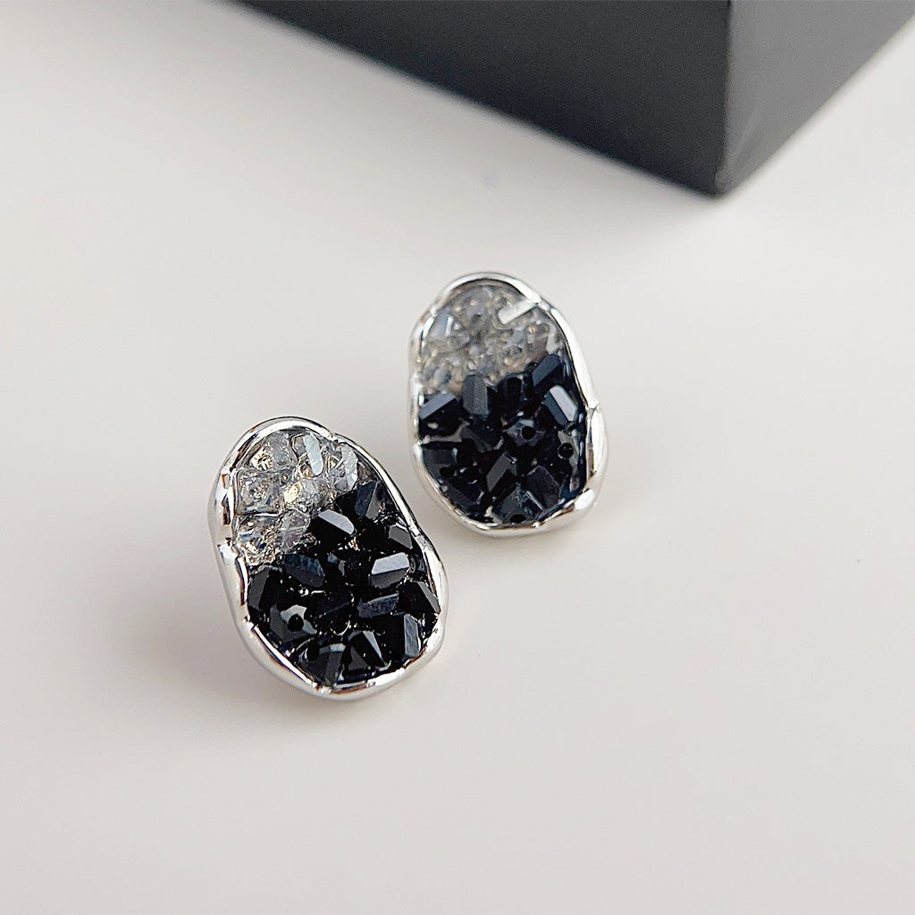 A pair of sparking oval stud earrings with a two-tone design of black and clear gradient crystals set in a silver-finished brass base.