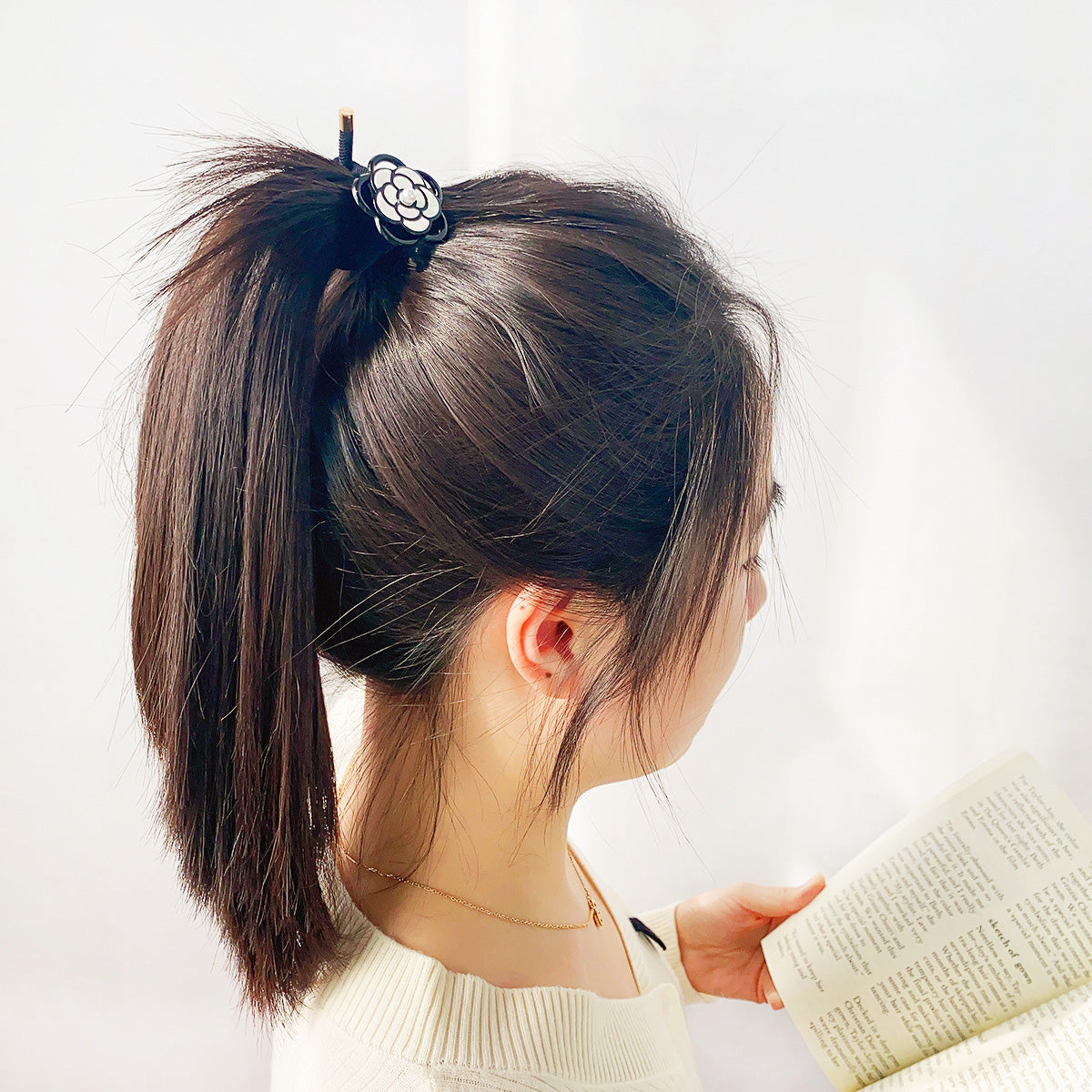 A close-up of a black hair tie with a white camellia flower accent, elegantly securing a person's ponytail.