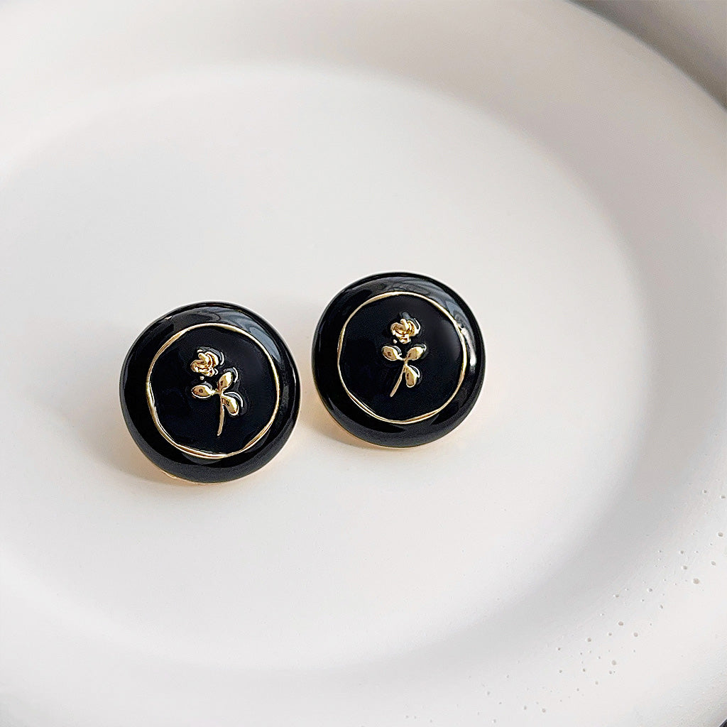 A pair of old school style round stud earrings featuring a delicate 14k gold flower pattern on a black enamel base.