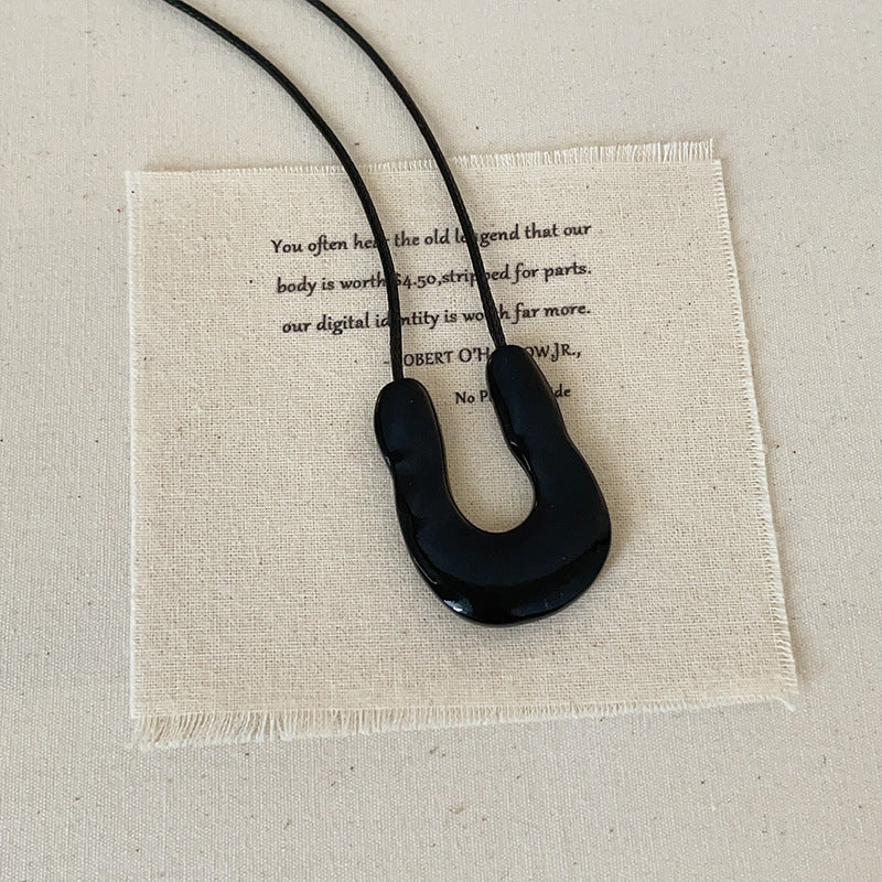A minimalist black U-shaped pendant on a black cord, displayed on a fabric background, representing modern statement fashion brass jewelry for wholesale.