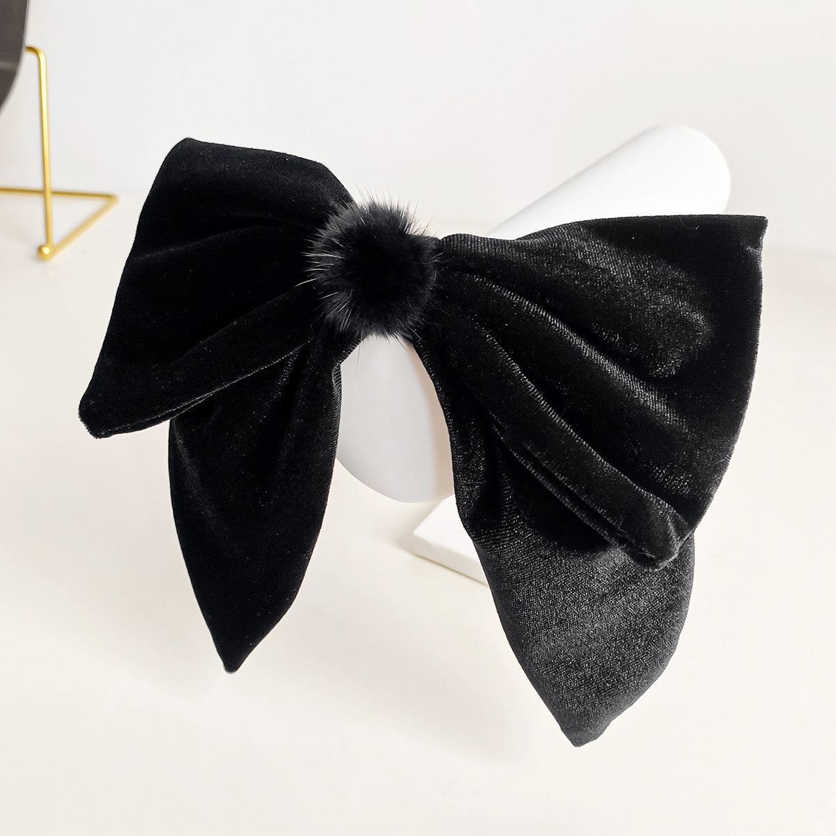 Close-up of a black velvet bowknot hair clip with a fluffy pom-pom center.