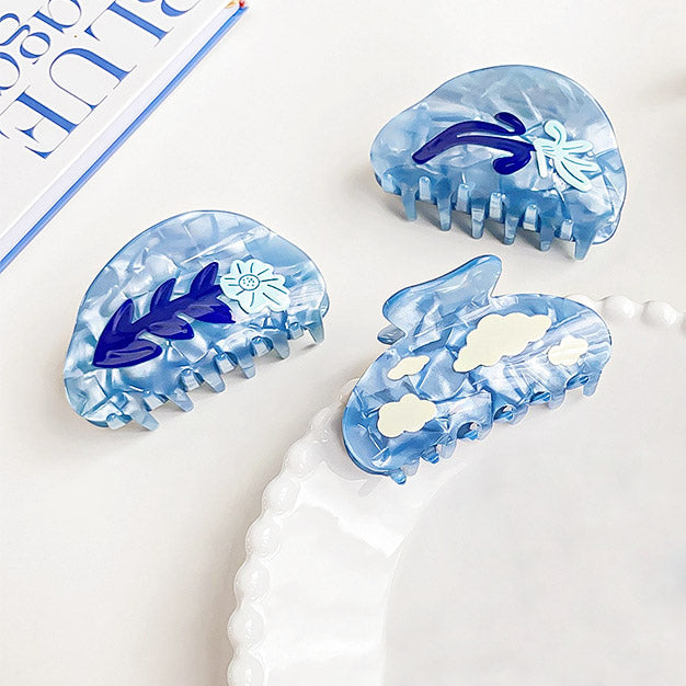 A collection of three stylish blue acetate hair claw clips with delicate white floral patterns, part of a wholesale set.