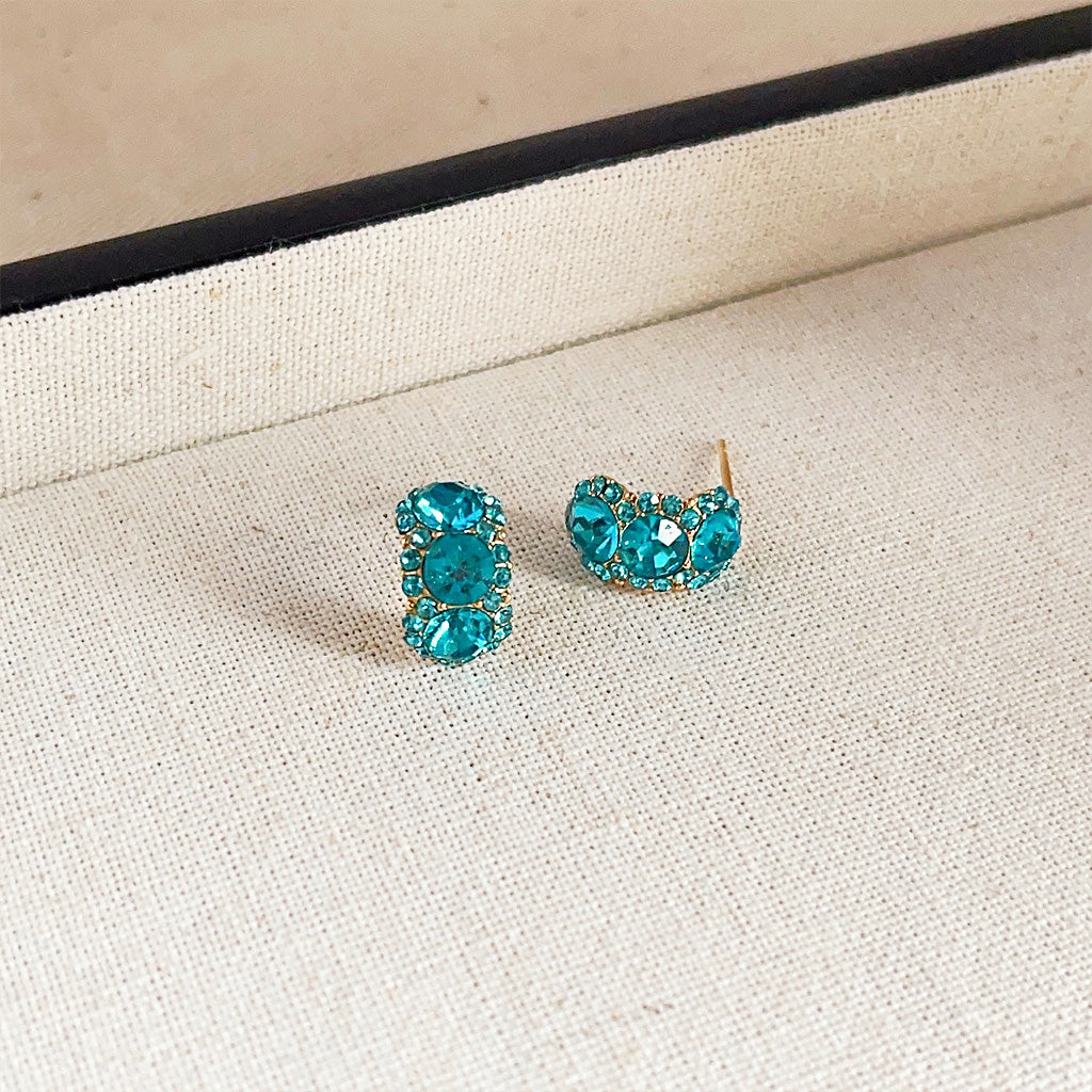 A close-up of the 14k gold-plated stud earrings, showcasing the brilliant blue rhinestone cluster design on a white background.