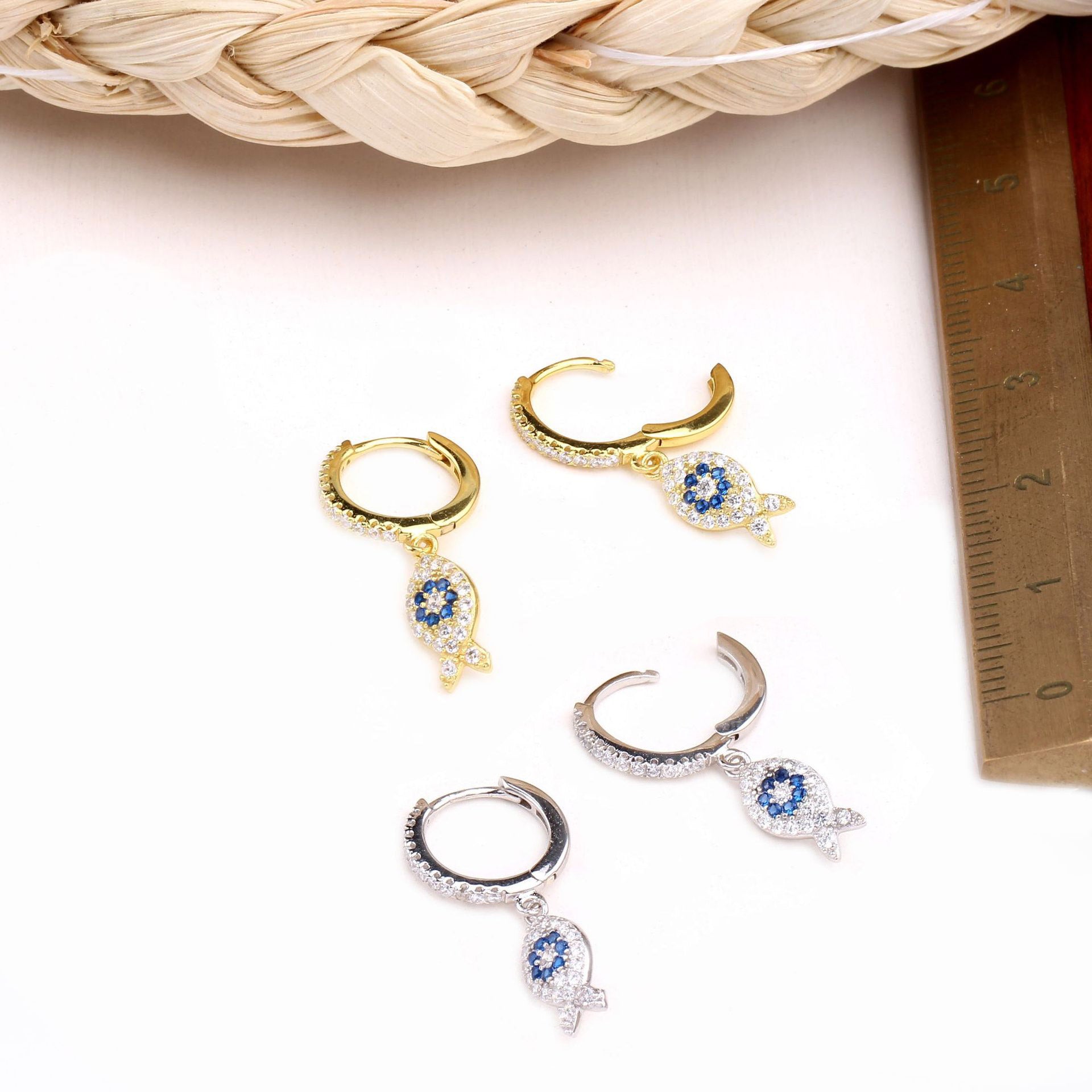 A collection of 925 sterling silver ocean fish huggie hoop earrings, showcasing both gold and silver finishes with intricate fish and leaf charms adorned with blue gemstones.