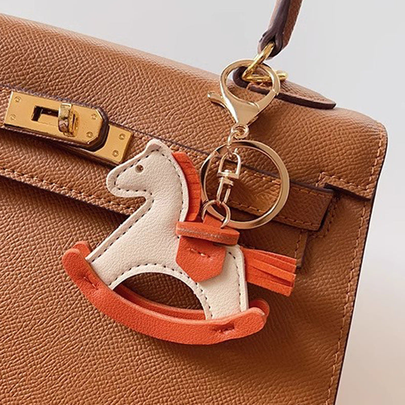 A stylish brown PU leather rocking horse keychain charm attached to the handle of a matching brown leather handbag, showcasing its use as a chic bag accessory.