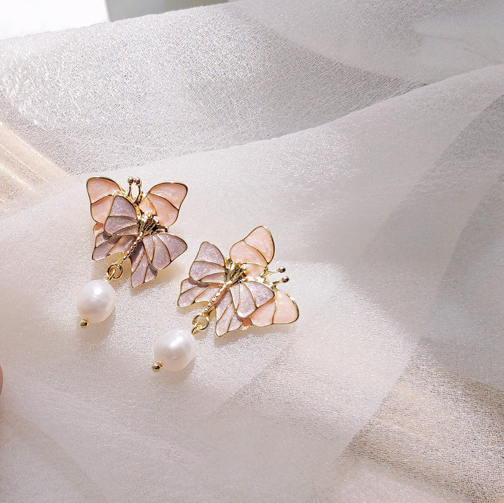 A pair of 14k gold-plated drop dangle earrings featuring a delicate purple butterfly motif and a lustrous freshwater pearl.