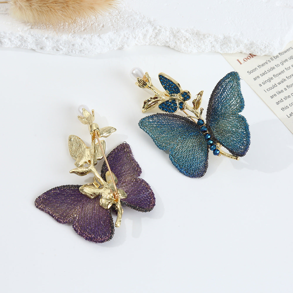 A set of luxury embroidered butterfly brooches, one in purple and one in blue, both featuring delicate fabric wings, faux pearl details, and gold-toned metal accents.