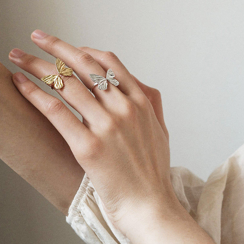 A model's hand showcasing two 925 sterling silver butterfly rings from the adjustable set, one in a silver finish and one in a gold finish.