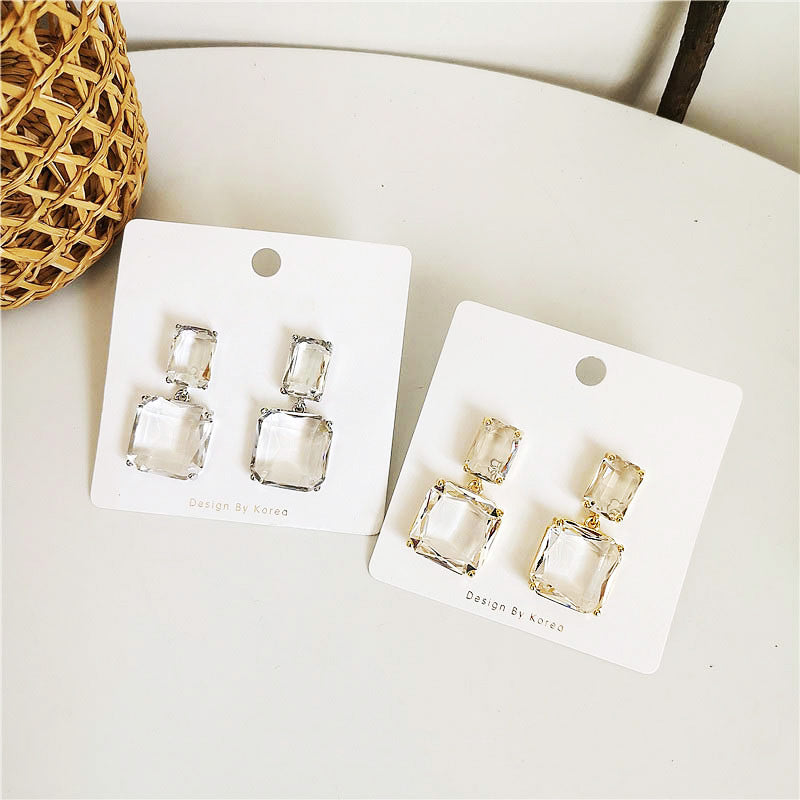 A pair of geometric square crystal drop earrings in a gold setting next to a pair in a silver setting, showcasing both available plating options.