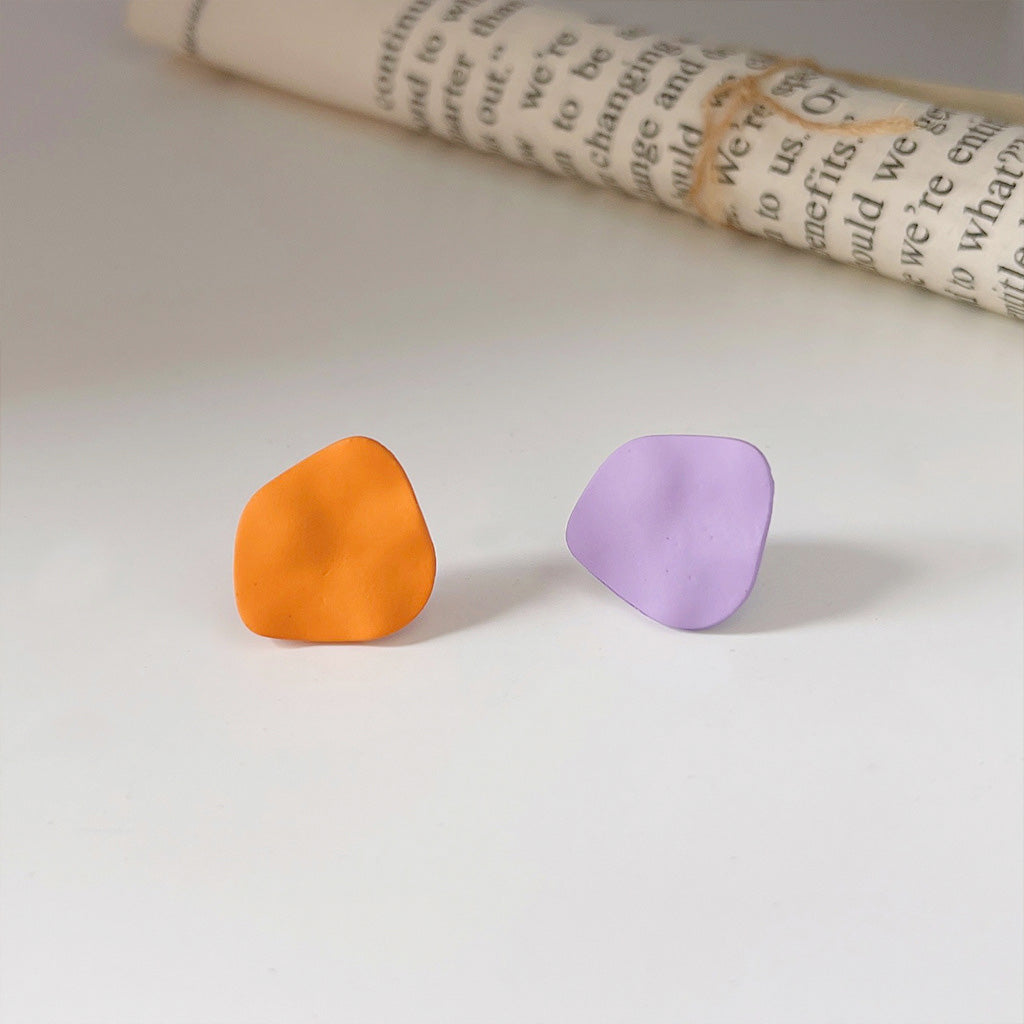A set of matte enamel stud earrings in irregular shapes, featuring one vibrant orange pair and one deep purple pair on a clean white background.