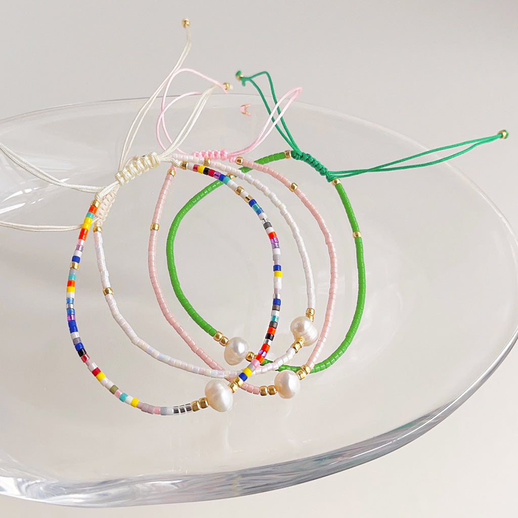 An artistic arrangement of colorful Bohemian rice bead and pearl handwoven bracelets displayed on a glass plate, showcasing the variety in the set.