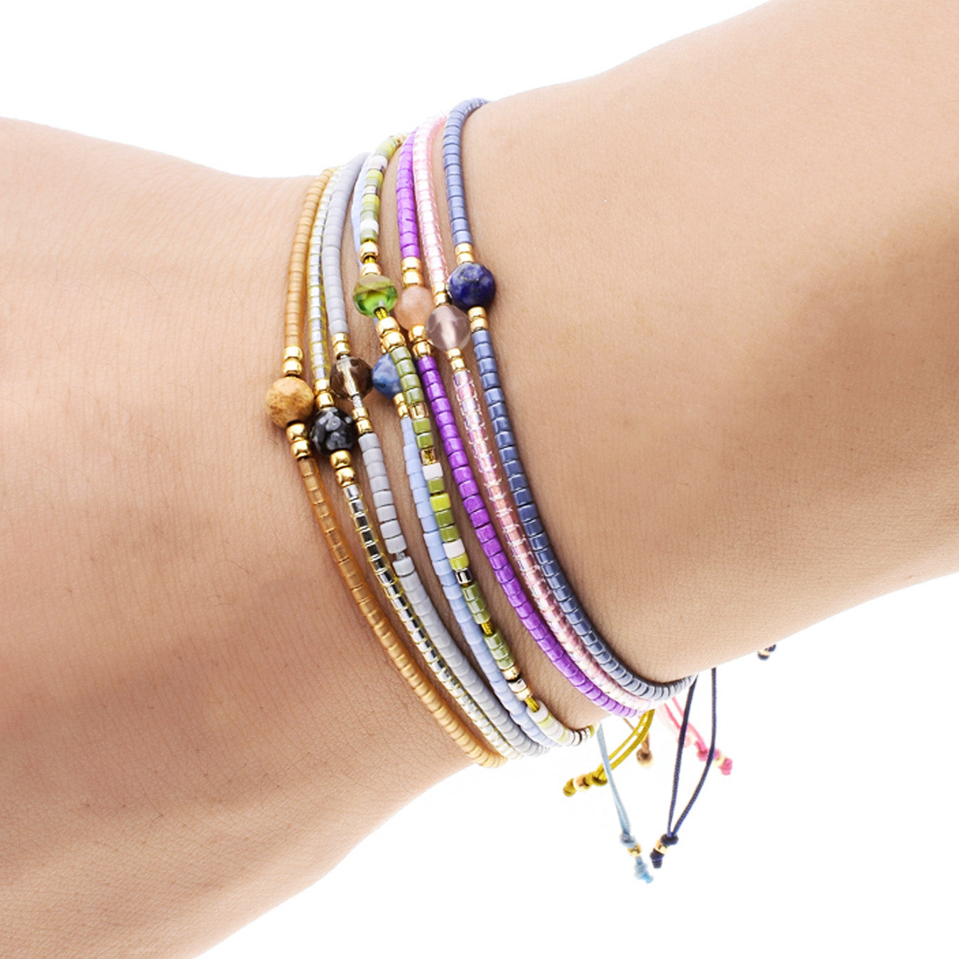 A stack of multi-color bohemian handwoven bracelets featuring small rice beads and natural stones, worn on a wrist.