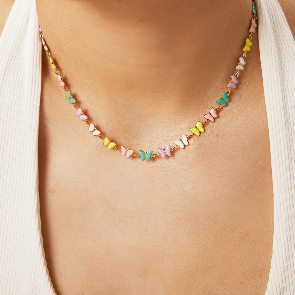 A close-up of a model wearing the stainless steel necklace with colorful enamel butterfly charms, highlighting its delicate design against a white top.