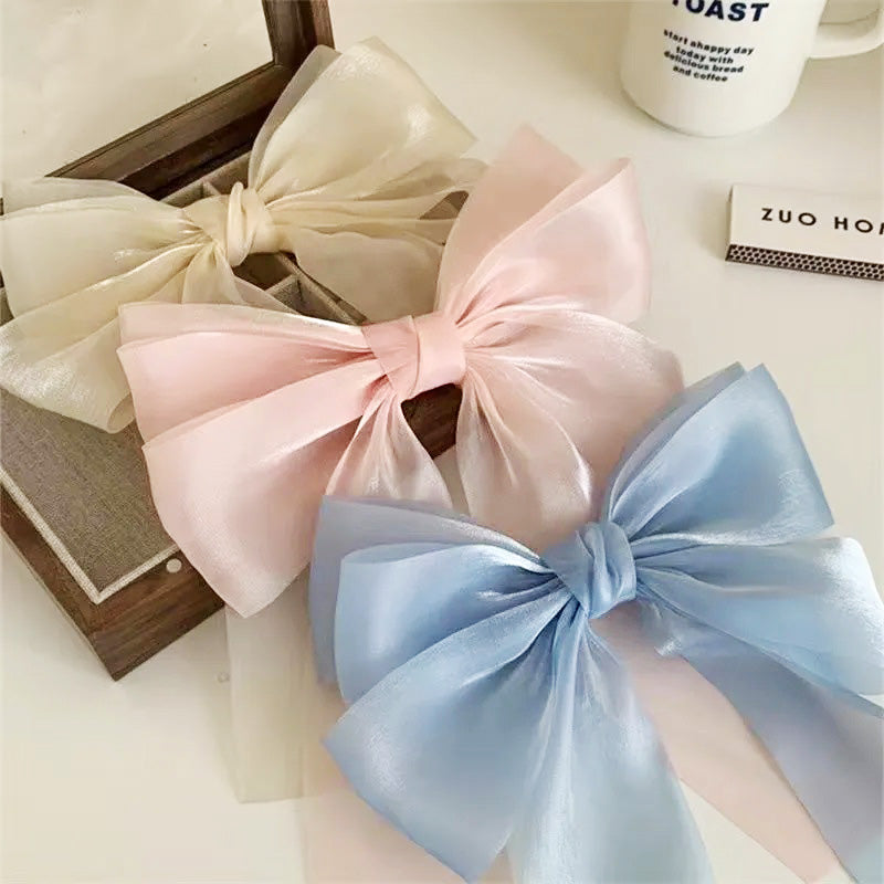 A set of three two-layer satin big bow knot hair clips in cream, pink, and blue, displayed on a neutral background.