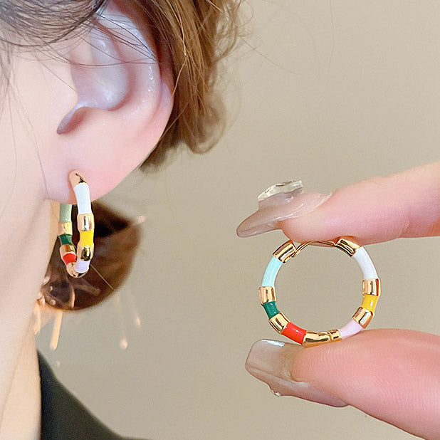 A vibrant pair of bulk brass hoop earrings featuring colorful enamel segments in red, green, yellow, white, and blue with elegant gold accents.
