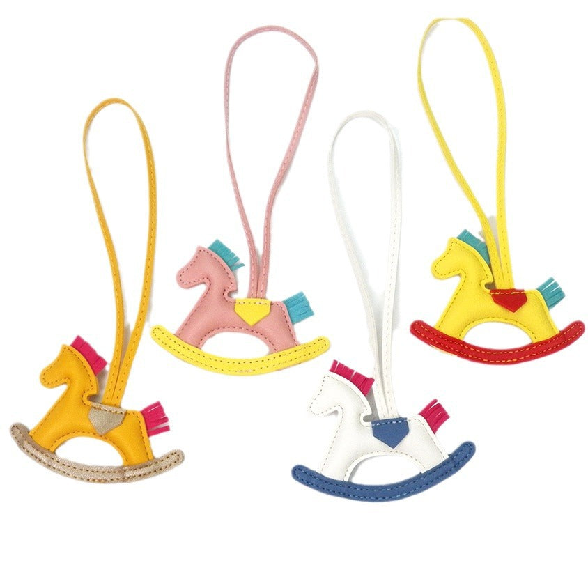 A collection of four colorful PU leather rocking horse keychains in yellow, pink, white, and red, showcasing the variety available.