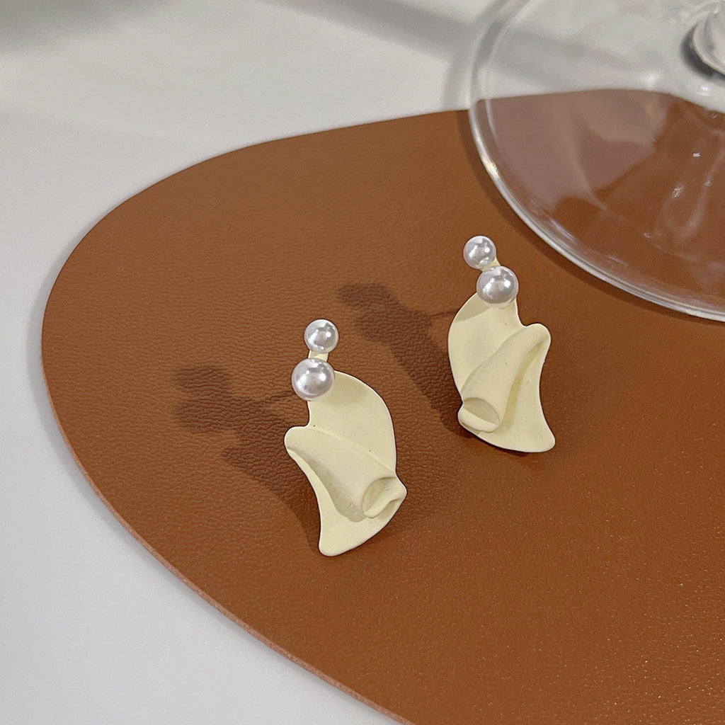 A pair of cream-colored stud earrings with an irregular folded design and a central pearl accent, part of the white enamel pearl earring set.