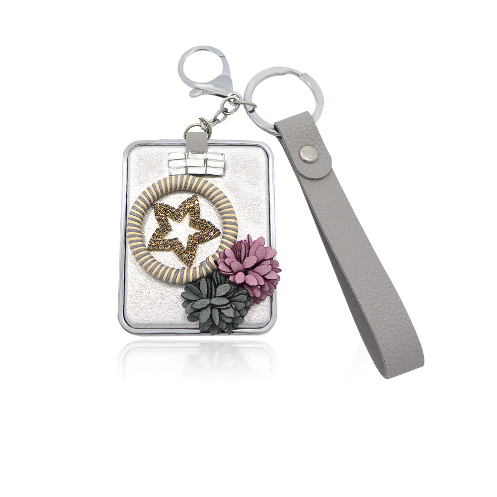 A stylish wrist strap decorated compact mirror, featuring an elegant rectangular case with a star and floral design.