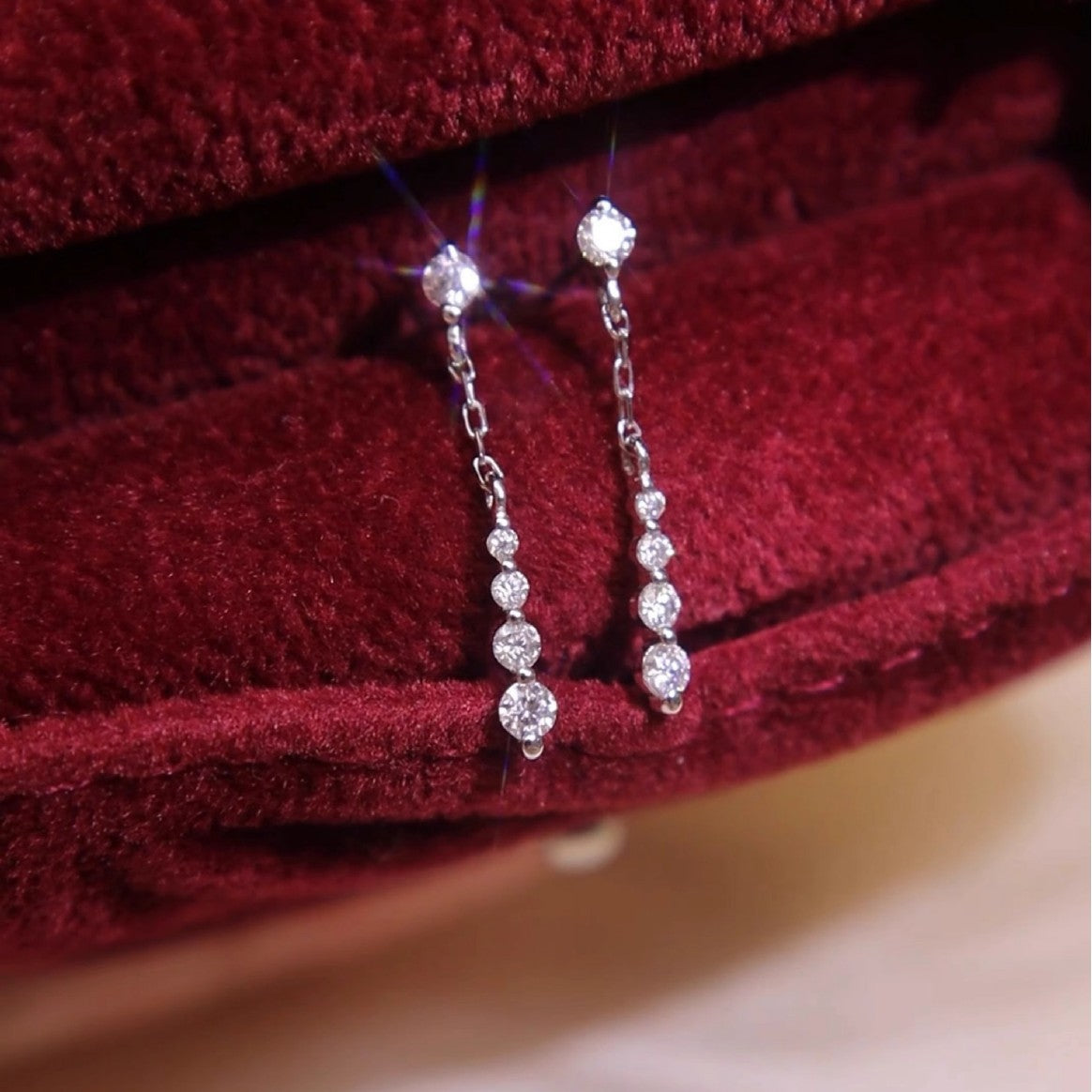 A pair of wholesale 925 sterling silver chain drop dangle earrings with sparkling cubic zirconia, plated in 18k white gold, displayed elegantly on a red velvet box.