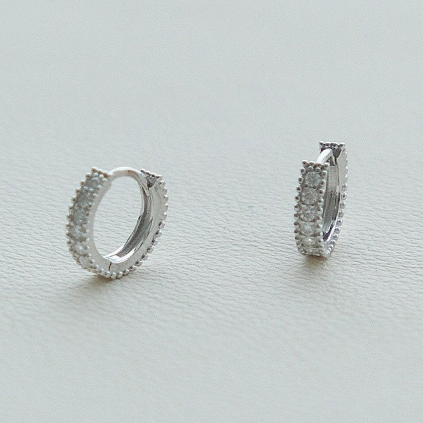 A pair of 925 sterling silver huggie earrings with platinum plating and a pave setting of sparkling cubic zirconia stones.