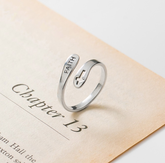 A 925 sterling silver ring engraved with the word 'FAITH' and a cross symbol, resting on an open book to showcase its inspirational design.