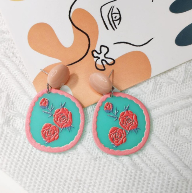 A close-up of Korean fashion cute flower acrylic earrings, featuring a floral design with red roses on a teal background. Style JRE-171.