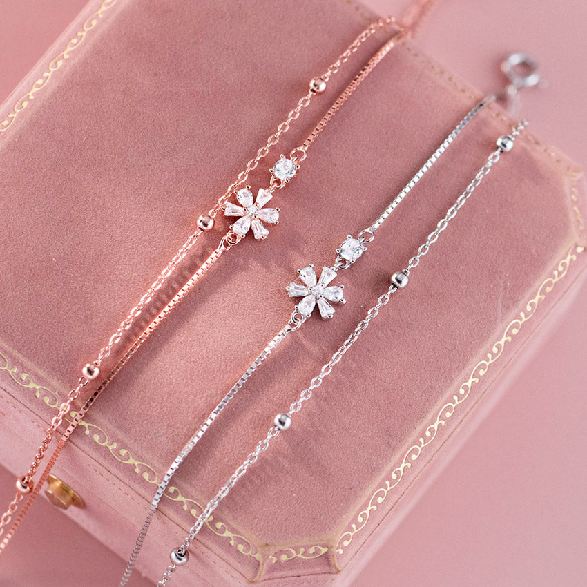 A set of three elegant 925 sterling silver bracelets with sparkling cubic zirconia flower charms, displayed in a pink jewelry box.