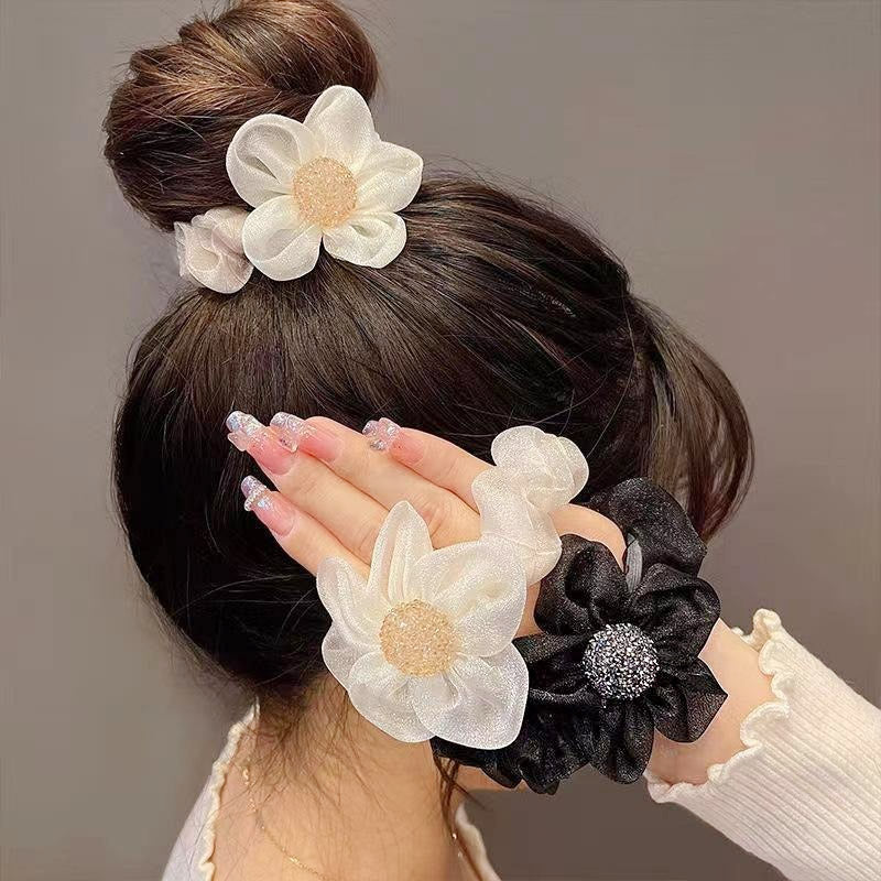 A set of elegant lace hair scrunchies with shiny organza flower designs, shown in both beige and black.