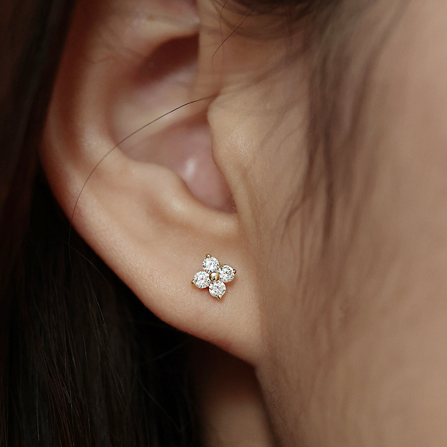 A close-up of a woman wearing a 925 sterling silver four-leaf clover stud earring, featuring sparkling zircon stones.