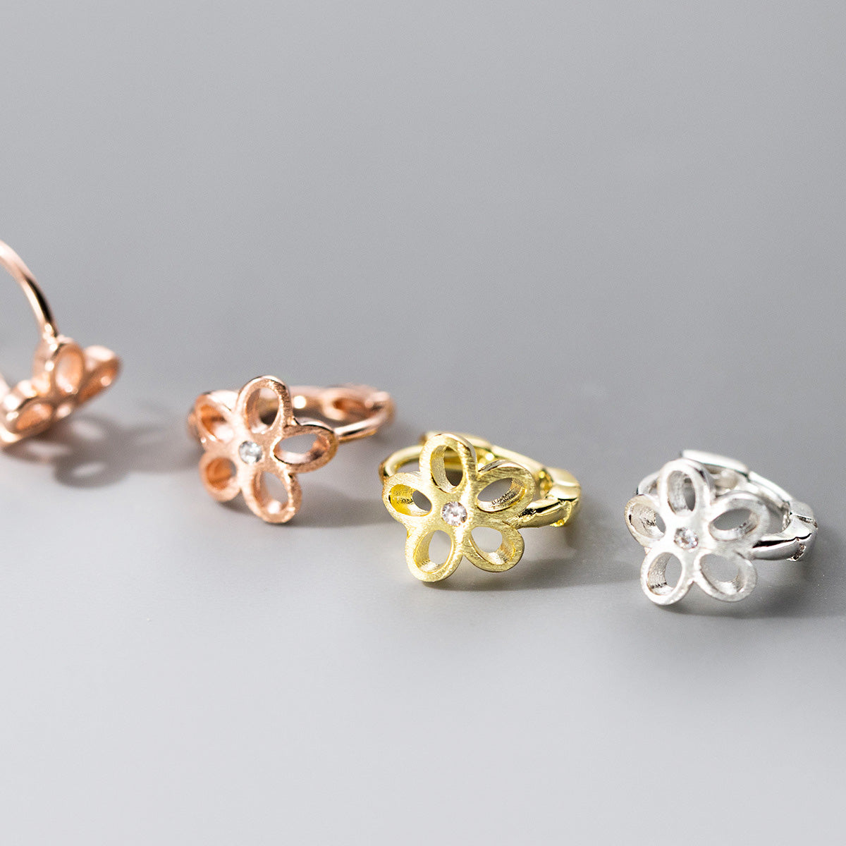 A collection of wholesale 925 sterling silver flower huggie hoop earrings displayed in rose gold, yellow gold, and silver finishes.