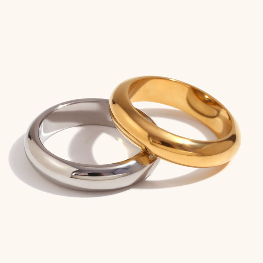 A minimalist product shot of two thick band rings, one in 18K gold finish and one in silver finish, made from polished stainless steel.