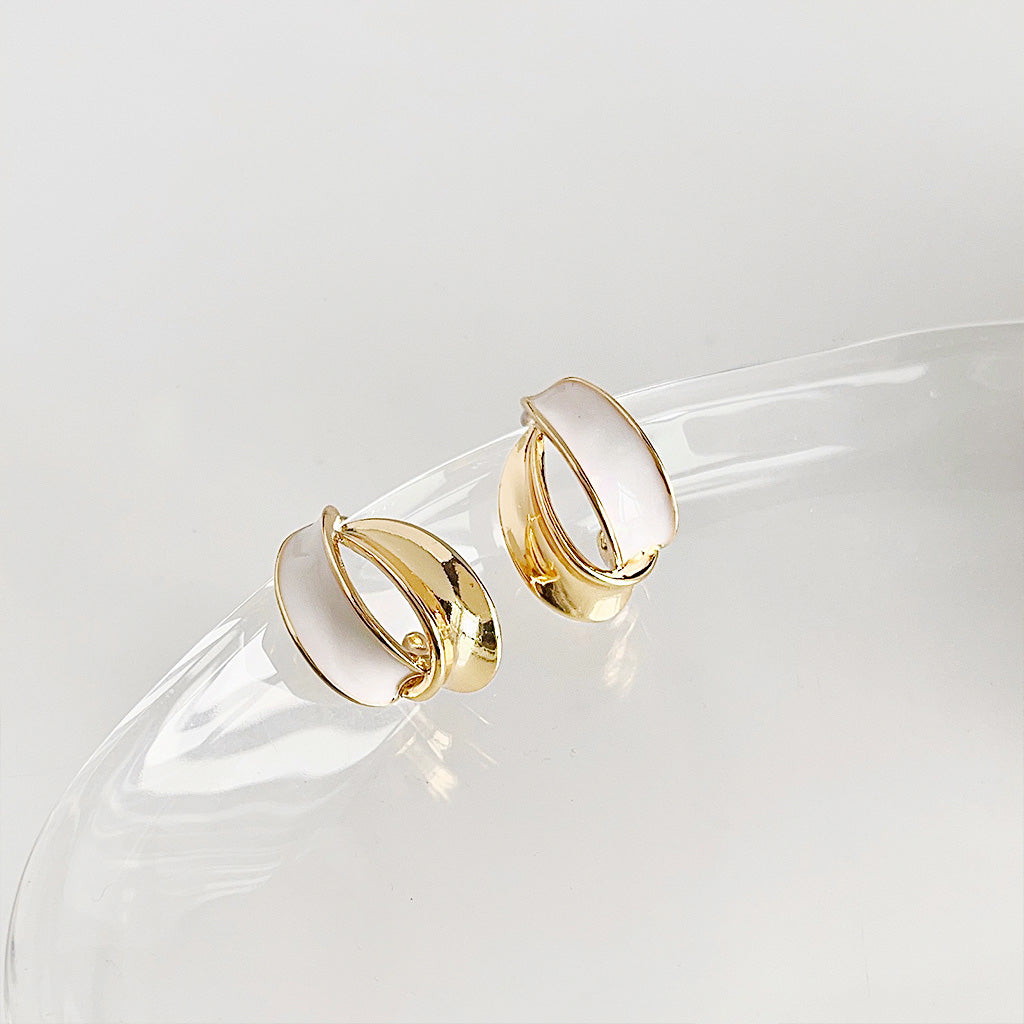 A set of five 14k gold-plated stud earrings with white enamel geometric designs, elegantly displayed on a transparent stand.