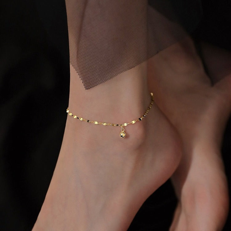 A close-up of a 925 sterling silver anklet in a gold tone, featuring a minimalist cat-shaped charm with a central blue cubic zirconia stone.