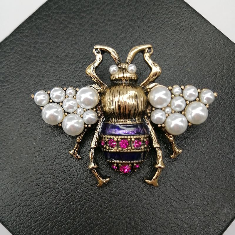 A detailed close-up of the Vintage Bronze Bee Brooch, highlighting its antique gold finish, faux pearl wings, and purple enamel body with magenta rhinestone accents.
