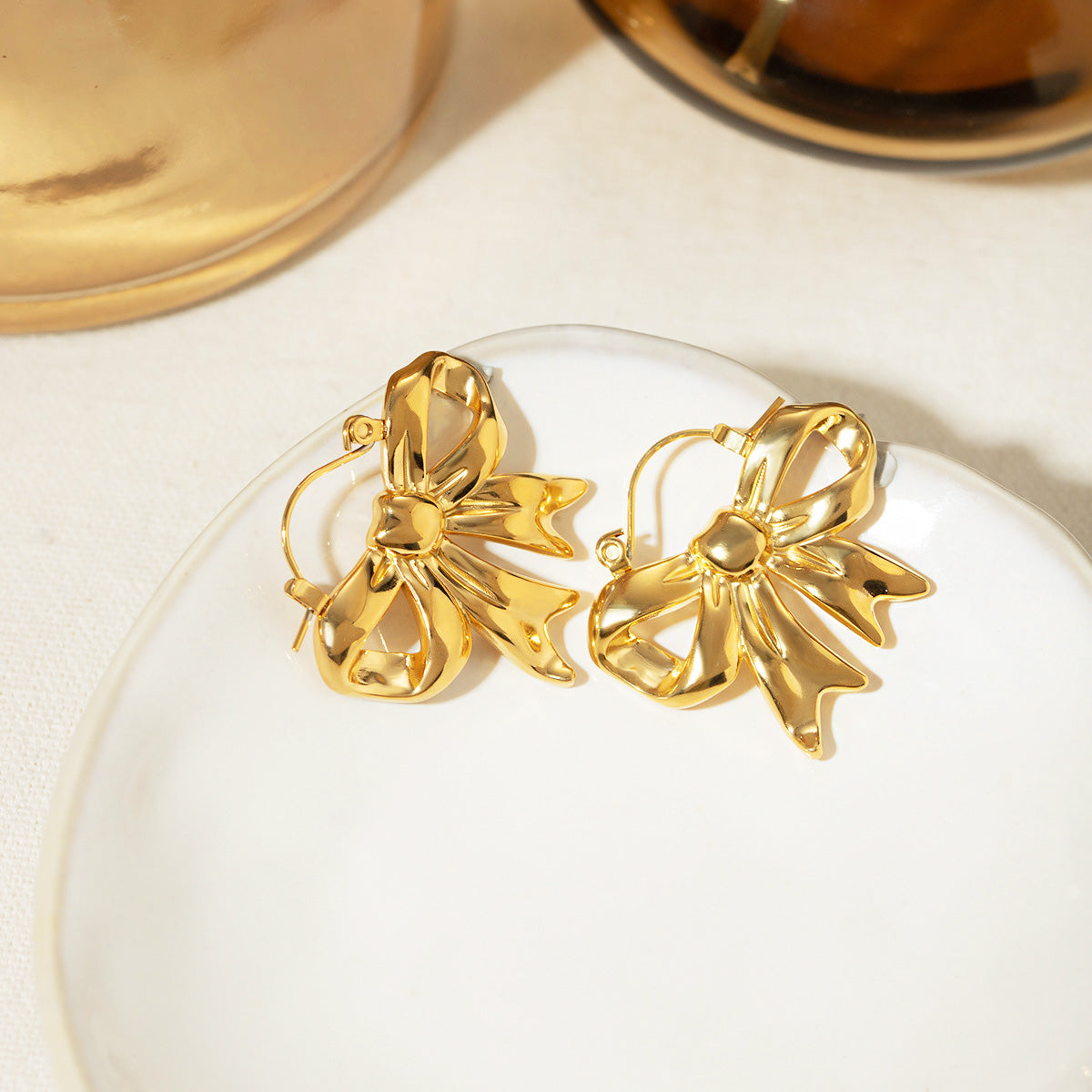 A pair of elegant gold-plated stainless steel earrings designed in a delicate ribbon bow shape, shown against a clean white background.