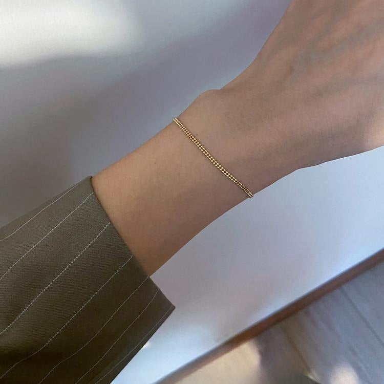 A woman's wrist adorned with the 925 Sterling Silver 14K Gold Plated Minimalist Double Layer Beaded Chain Bracelet.