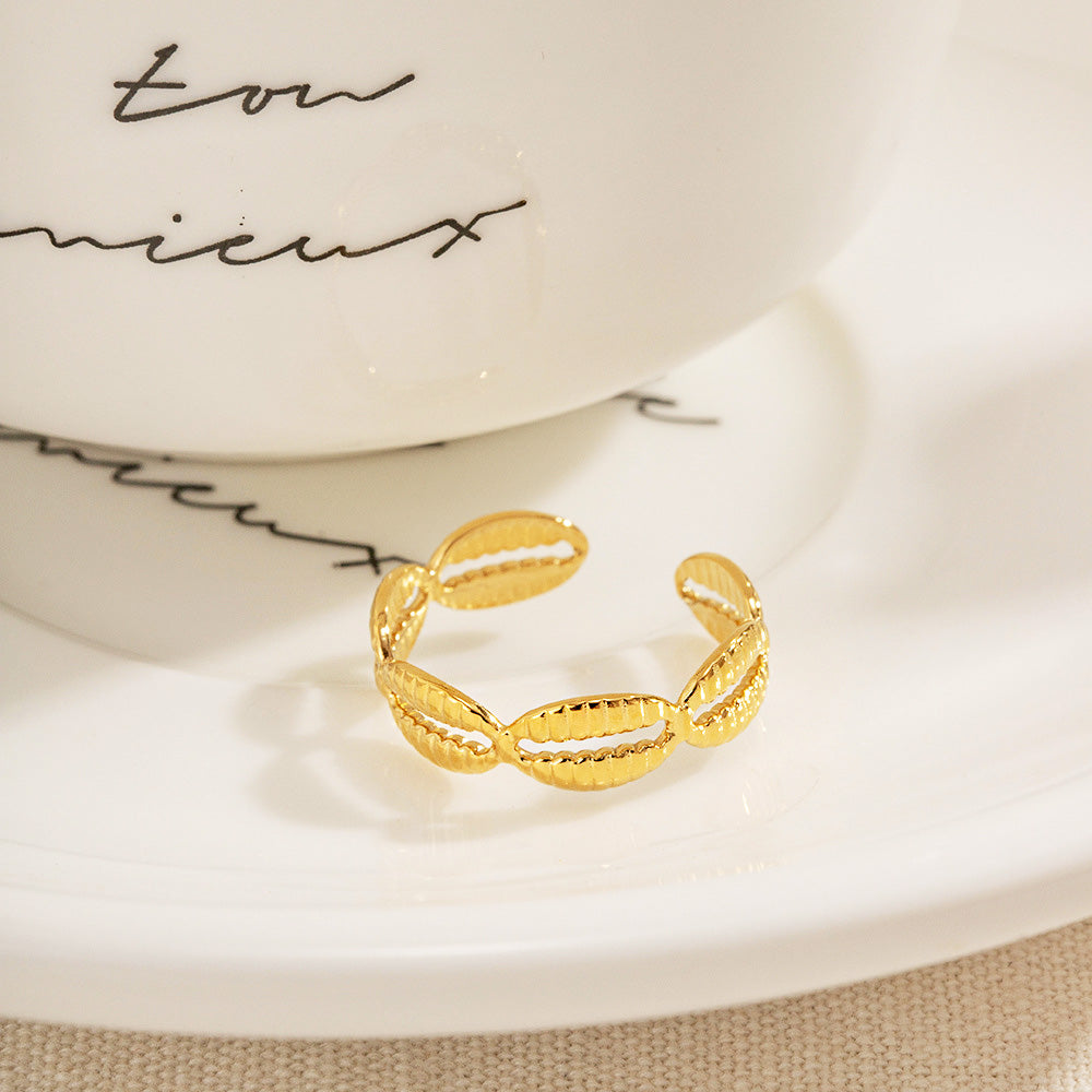 A set of five stainless steel gold-plated cowrie shell open rings displayed elegantly on a white saucer.
